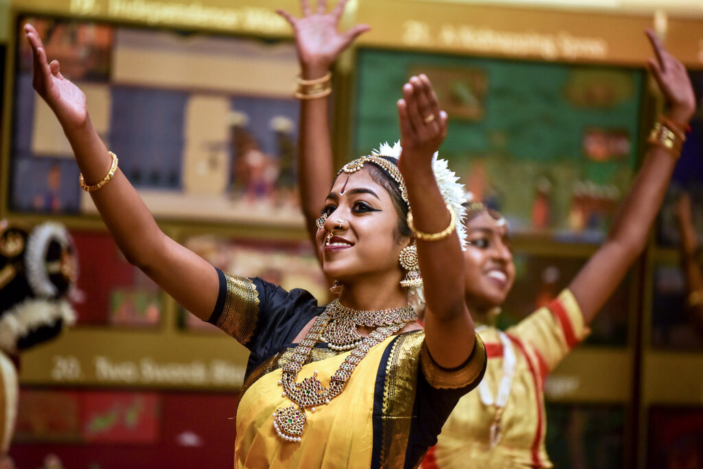 Two dancers in traditional Tamil dress dance happily with arms raised.