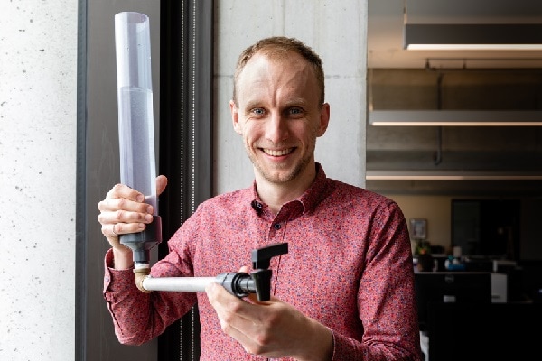 David Taylor smiles as he holds up a plastic tube attached to a pipe ending in a spigot.