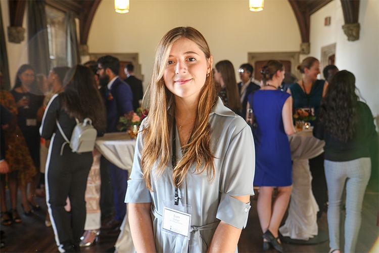 Ecem Sungur smiles while taking part in a social reception in a large hall.