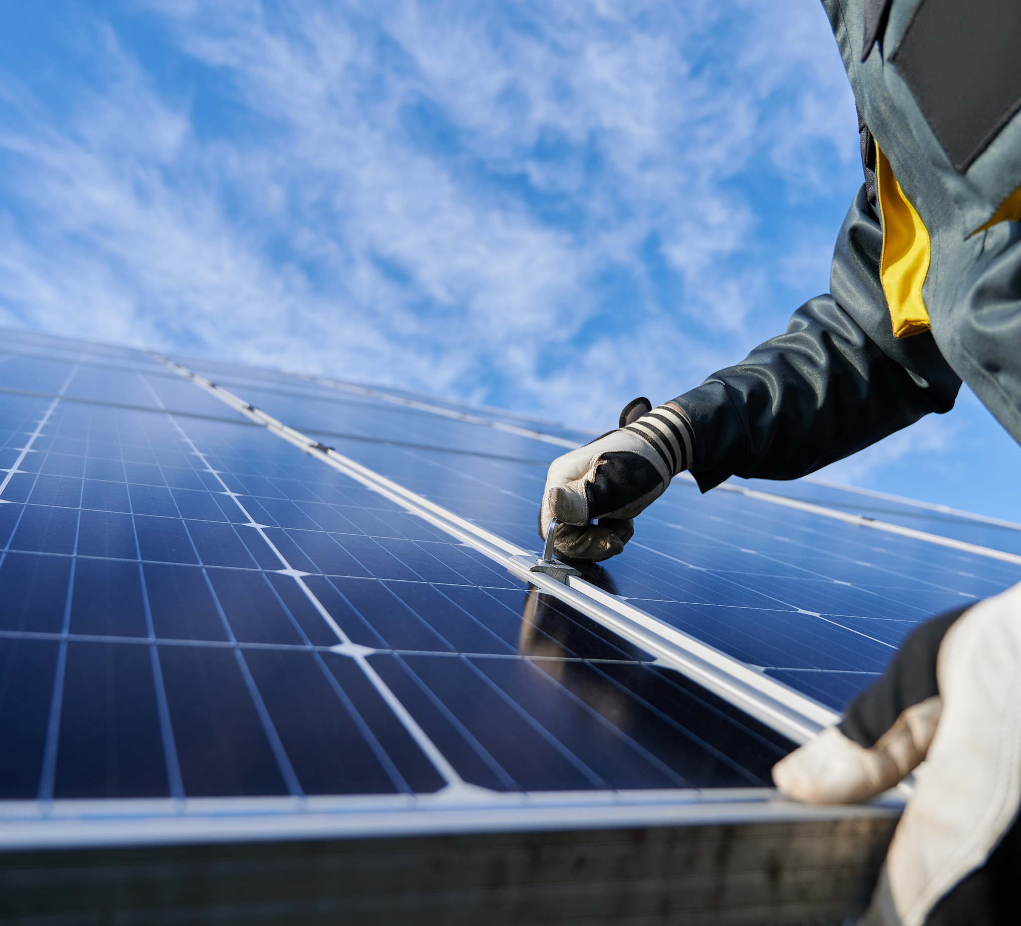 A person wearing protective gloves adjusts a fastening on a solar panel.
