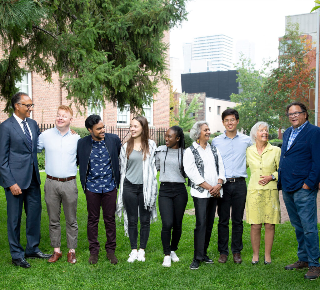 People of diverse ages, races and genders laugh together as they stand side by side on a lawn outside Innis College.