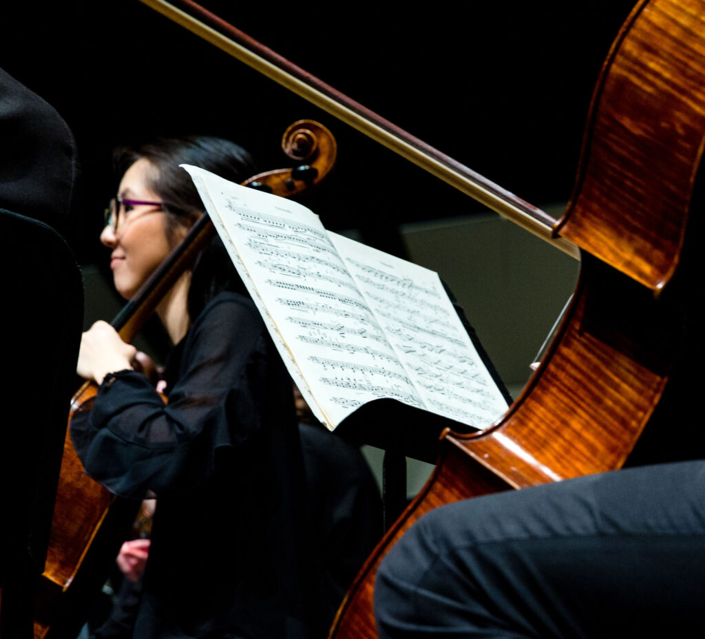 An image of part of a string orchestra, showing sheet music on a stand in front of a cello player.