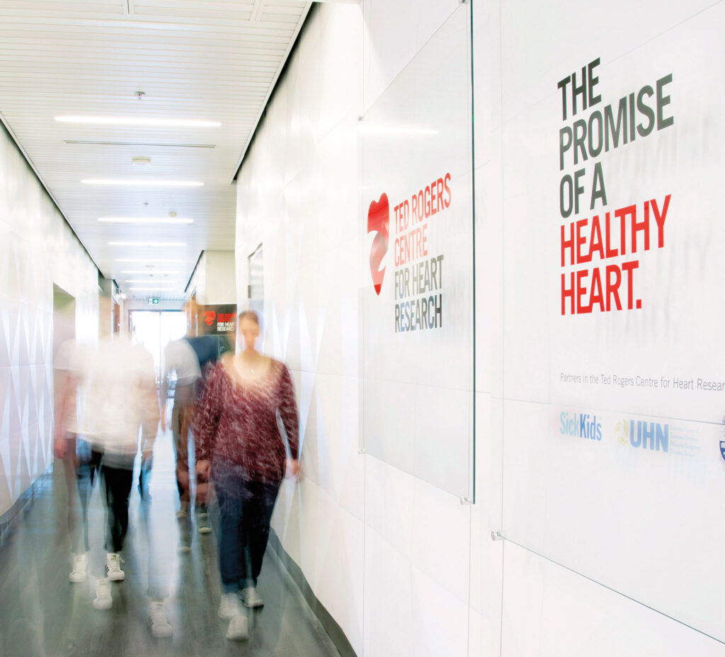 People walk down a hallway past signs that read: Ted Rogers Centre for heart research and the promise of a healthy heart.