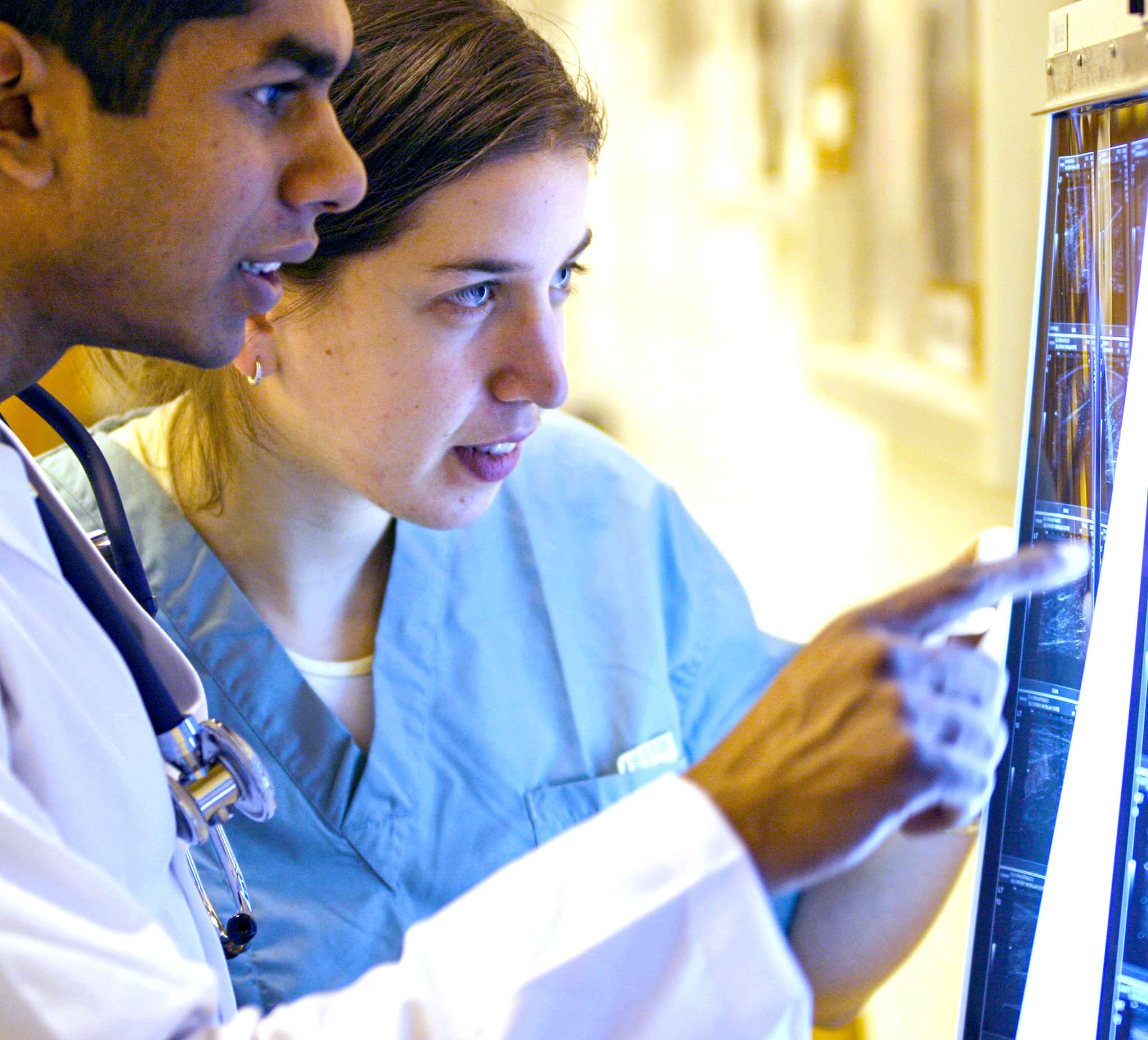 Two medical students, wearing scrubs and stethoscope, examine a grid of x-ray images.