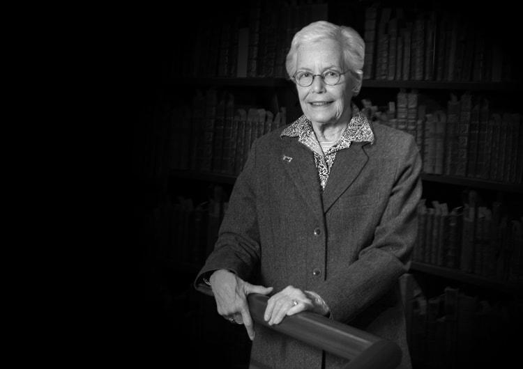 Katherine Morrison smiles, standing by a railing inn a library.