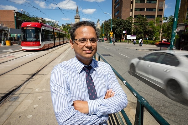 Khandker Nurul Habib smiles as he stands on a streetcar platform in the middle of busy Spadina Avenue.