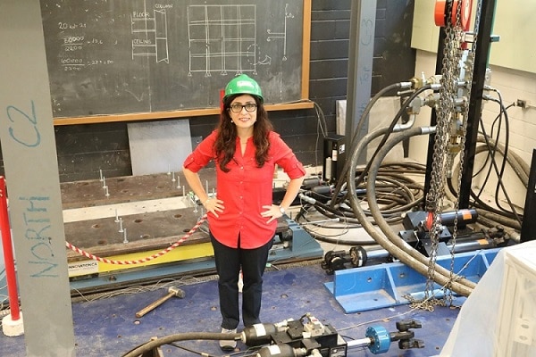 Oya Mercan smiles, standing surrounded by pipes, chains, valves, girders, a hammer and a chalkboard covered with diagrams.