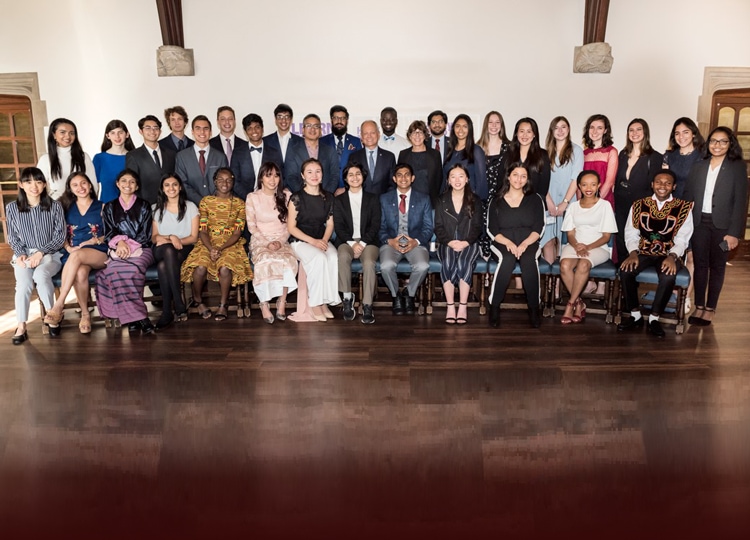 36 young students from all over the world smile, posed in two rows inside a large hall.