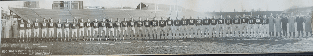 In this 1959 photo, 26 men in football uniform stand in a line across a football field.
