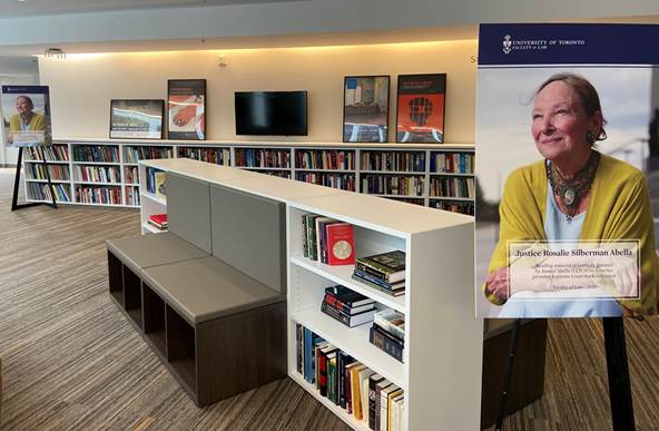 A poster of Rosalie Silberman Abella hangs beside low bookshelves. The shelves are full of books and grouped around a bench.