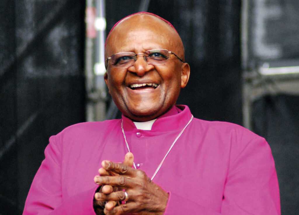 Archbishop Desmond Tutu laughing, with fingers clasped.