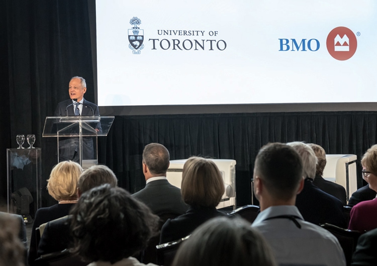 Meric Gertler stands at a podium beside a banner with the logos of BMO and the University of Toronto.