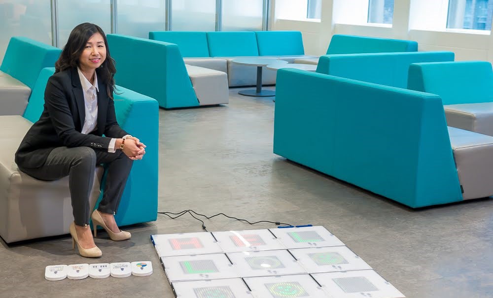 Charlene Chu next to the MouvMat: ten binder-sized tiles arranged in a grid with a display of five lights to the side.