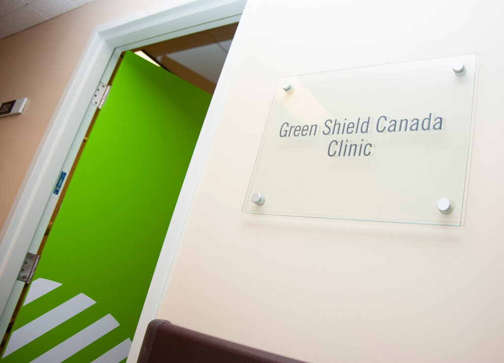 An open door painted green beside a sign that reads: Green Shield Canada Clinic.