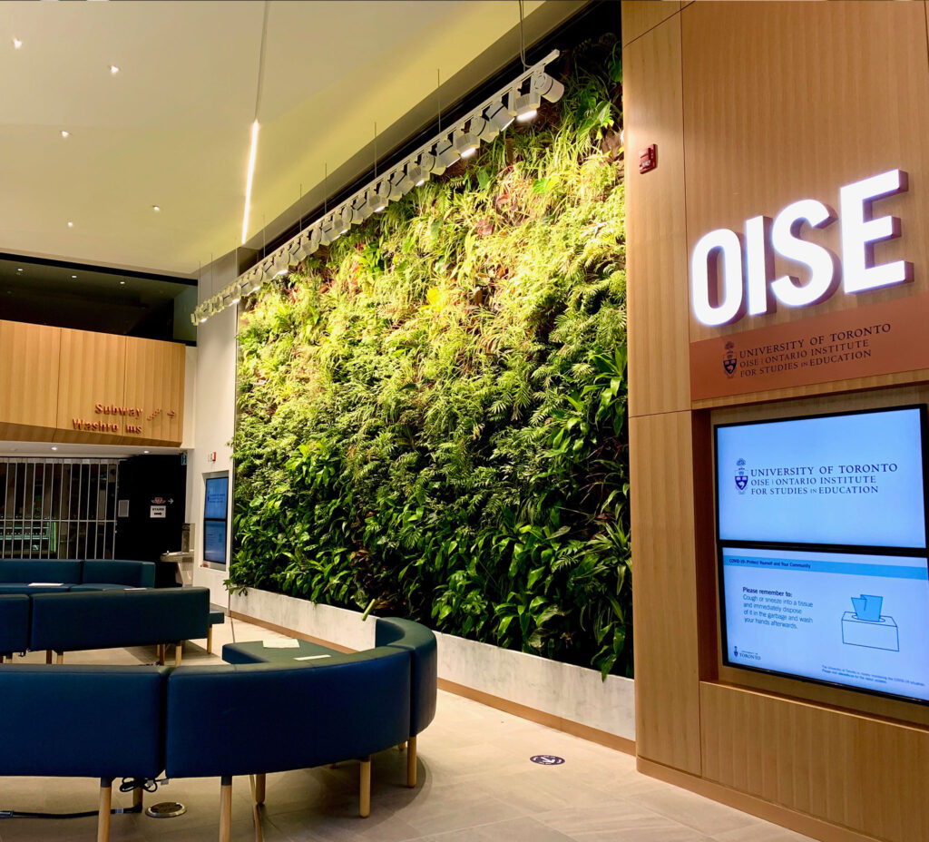 A lobby with curved and padded benches and one wall covered in growing plants. A big sign reads: O.I.S.E.