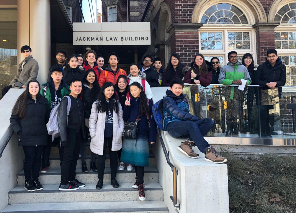 A group of teenagers smile and pose for a picture on the steps of the Jackman Law Building.