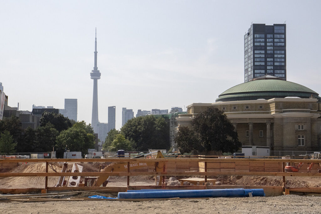 Behind a fence, a backhoe digs a large hole on U of T's Front Campus.