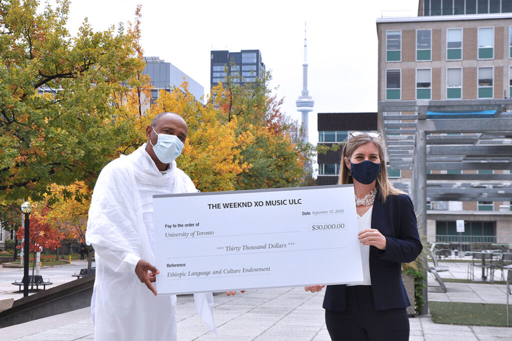 Tessema Mulugeta and Melanie Woodin hold a large-sized cheque for $30,000, made out from The Weeknd to U of T.