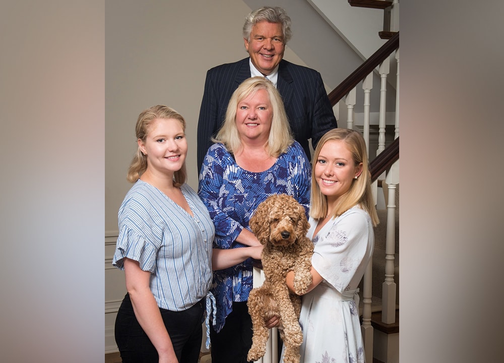 The Nesbitt-Lawlor family smiles as they stand on the staircase of their home with their puppy.