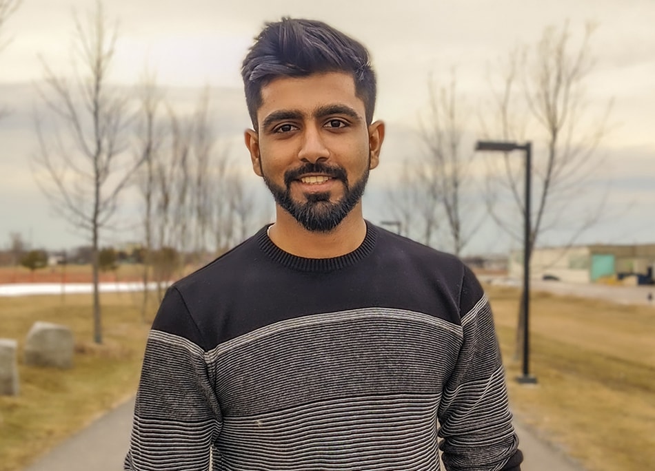 Rajasekar Dhanasekar smiles as he stands on a walkway outdoors.