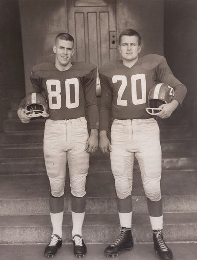 In a 1961 photo, Ron Crawford and Doug Boyd stand wearing football uniforms and holding their helmets under their arms.