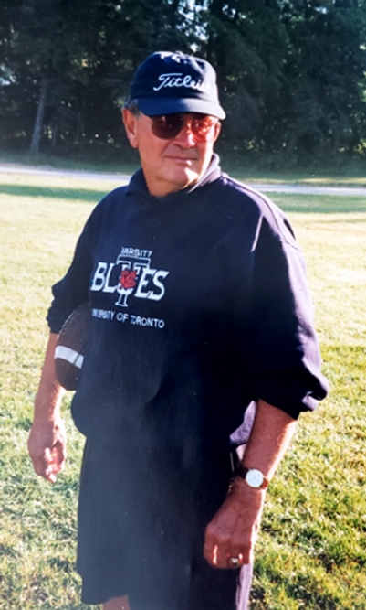 Ron Crawford stands on a grassy field wearing a Varsity Blues sweatshirt and holding a football.