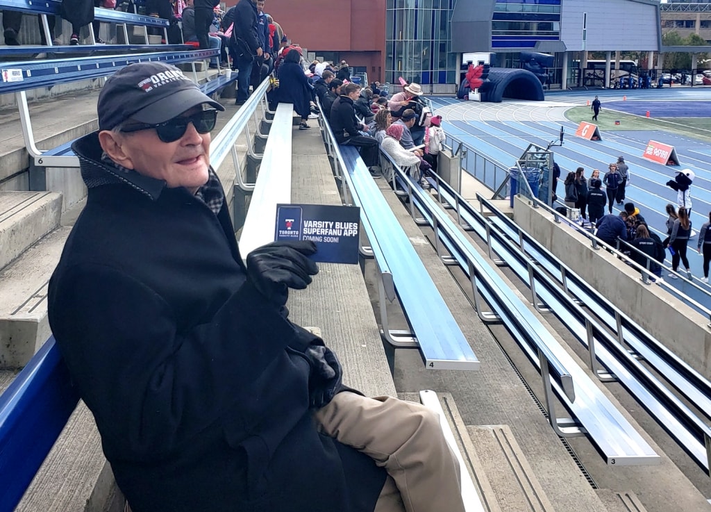 Ron Crawford sits in the stands at Varsity stadium and holds up his Varsity Blues Superfan pass.