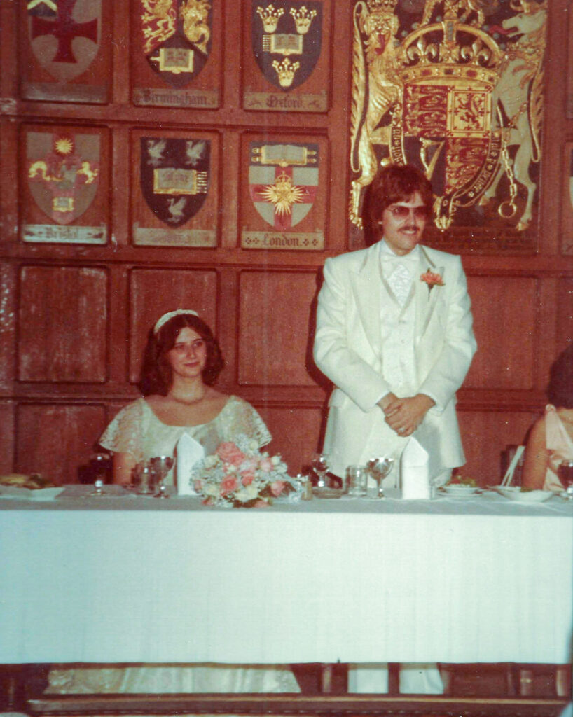 Thelma and Larry Beam, wearing wedding clothes, smile as they sit behind a banquet table in Hart House Great Hall in 1979.