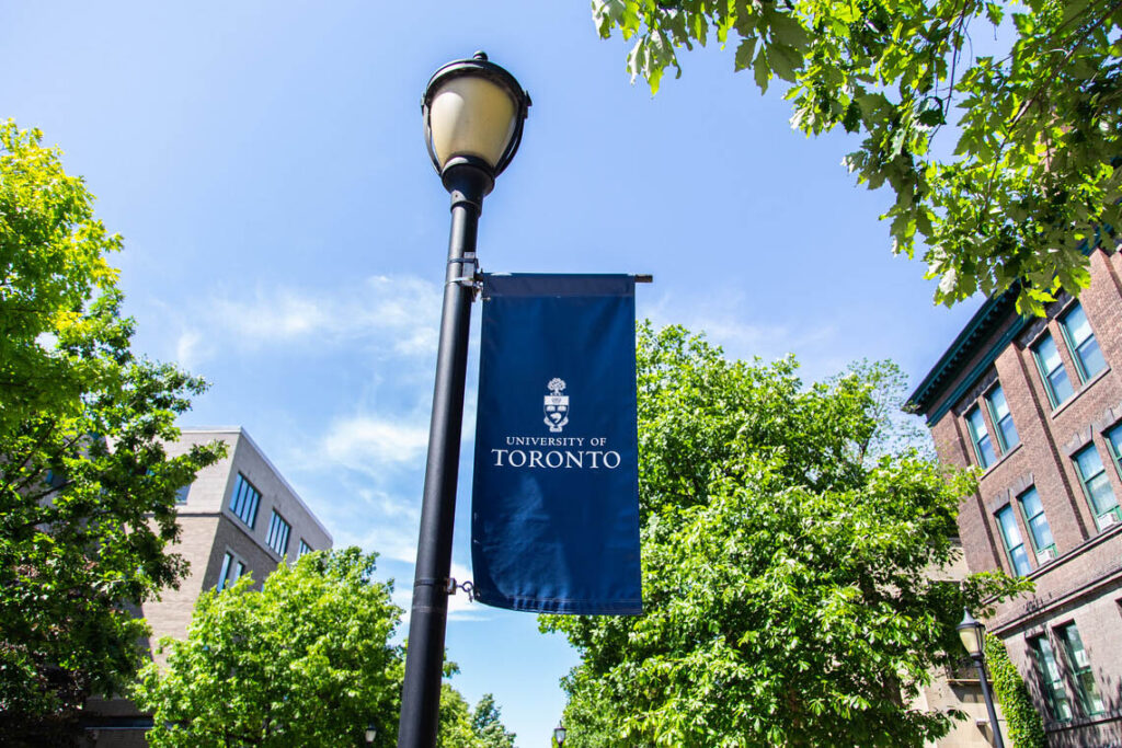 A banner reading University of Toronto hands from a lamp-post in front of a sunny sky.