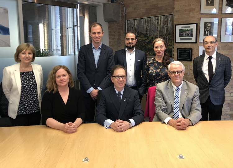 A smiling group of eight people, with Michael Dan at the centre, gather round a conference table.