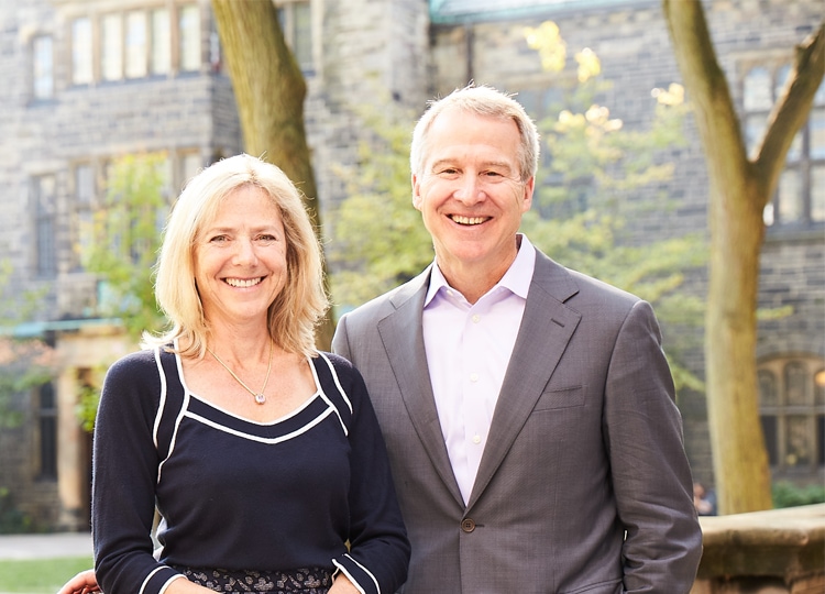 Joannah and Brian Lawson laugh as they lean on a stone railing in the Trinity quad.