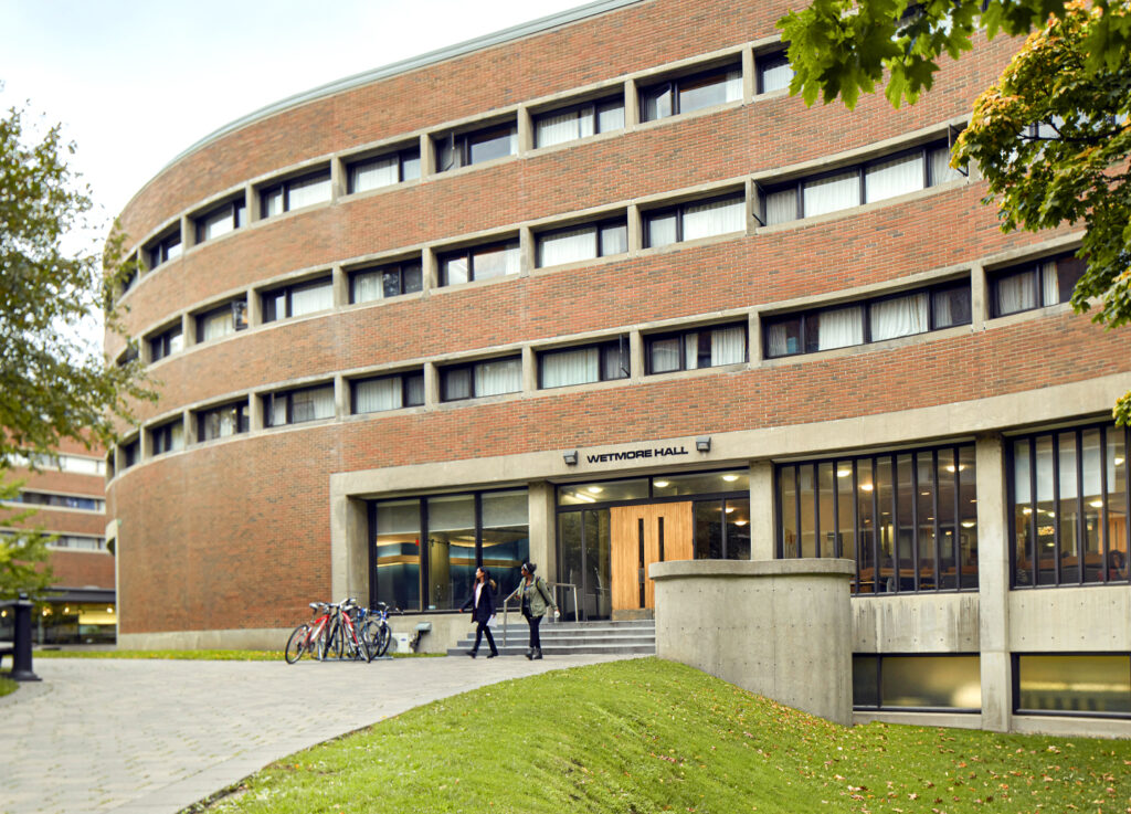 Two students walk out of Wetmore Hall, a New College residence with a distinctive curved facade.