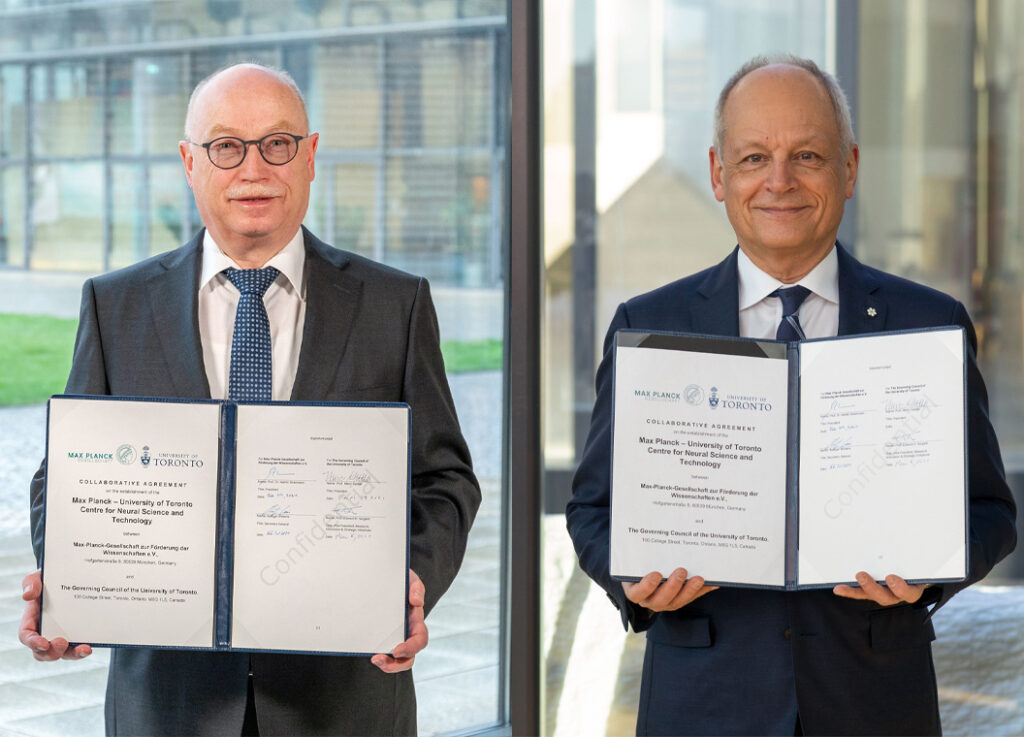 Martin Stratmann, Meric Gertler each hold a signed agreement. The images give the illusion of standing side by side for real.