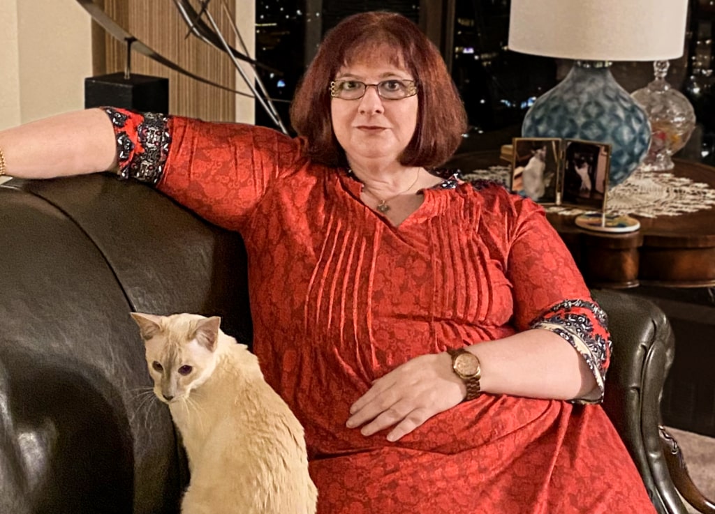 Thelma Beam, wearing colourful dress, sits on a sofa with a cat.