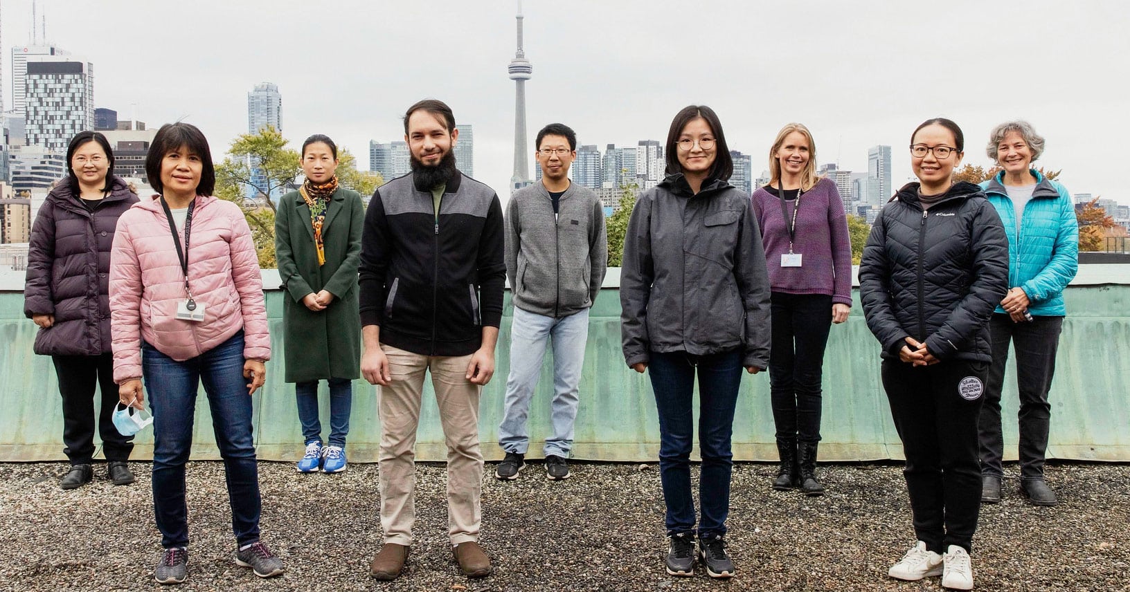 Nine people stand together on a rooftop. The CN Tower is visible behind them.