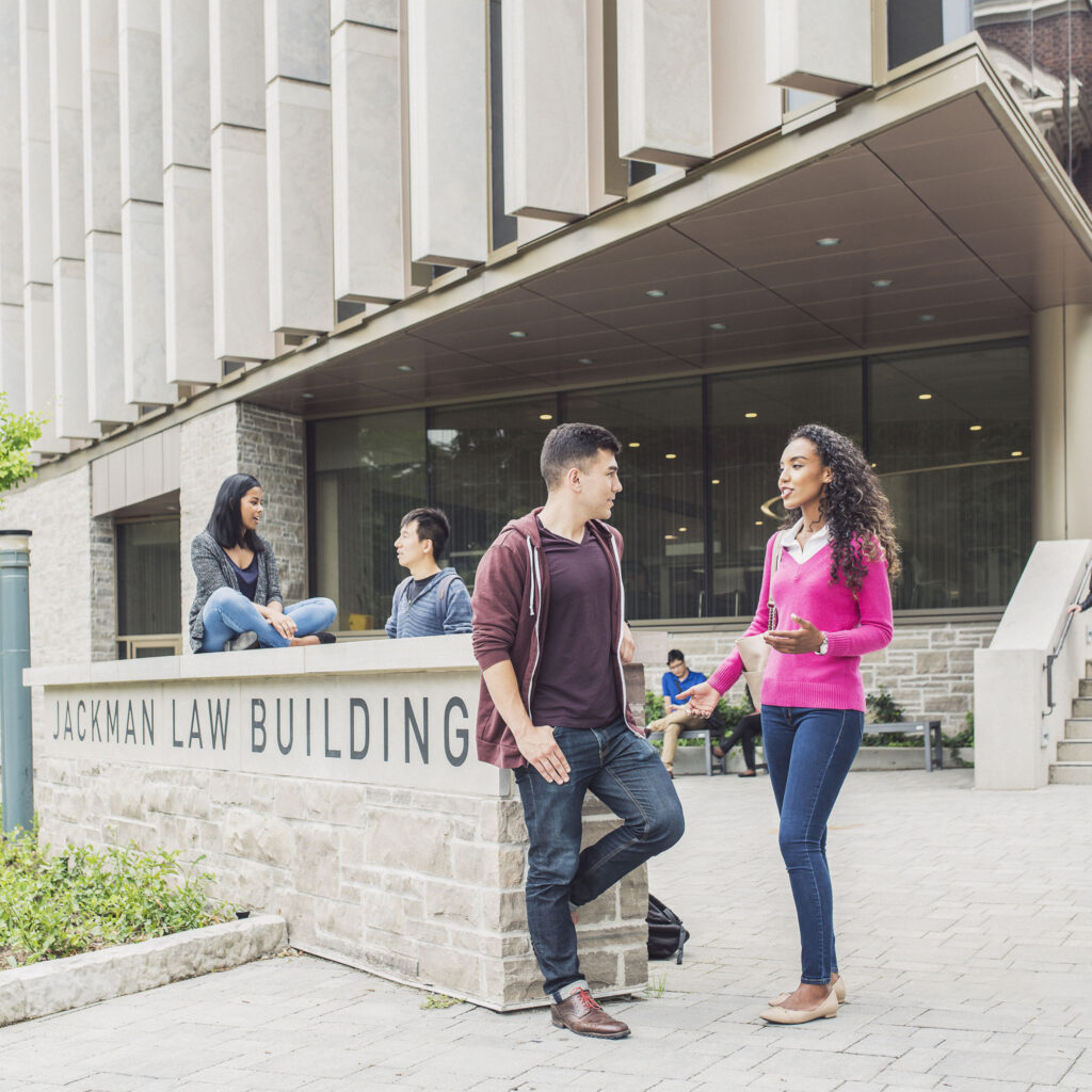 Students chat beside a stone wall with carved letters, they read Jackman Law Building.