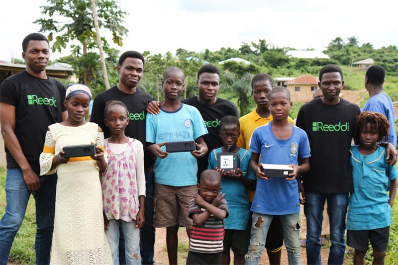 Children holding rectangular Reeddi capsules pose for a picture with entrepreneurs wearing Reeddi T-shirts.