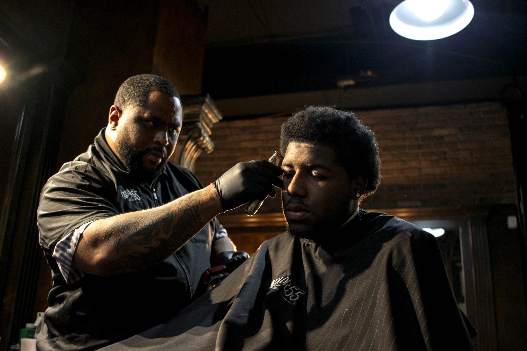 A Black barber shaves the temple of a Black man in a barber shop