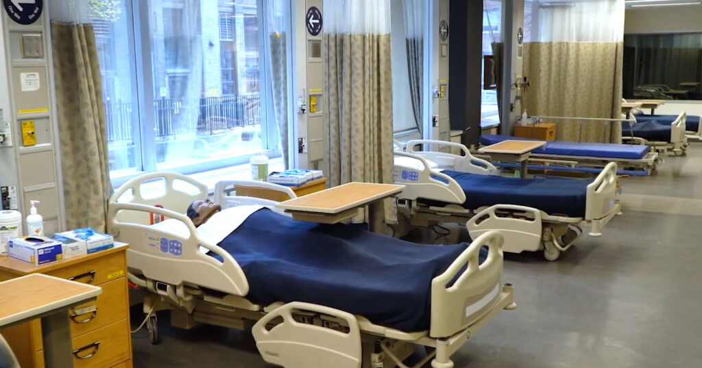 In the Bloomberg Nursing Simulation Lab, a row of hospital beds contain patient mannikins.