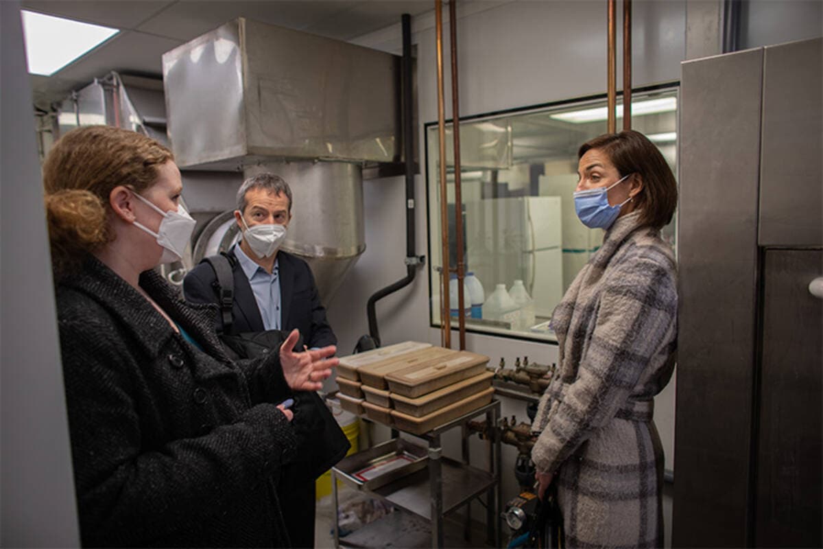 Three people wearing masks chat together as they view a laboratory.