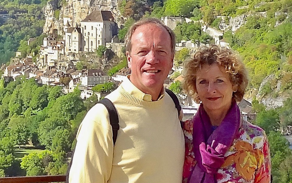 David and Louise Brace at a lookout point in David and Louise Brace in Rocamadour, France. Behind them, buildings cling to the sides of a steep rocky hill.
