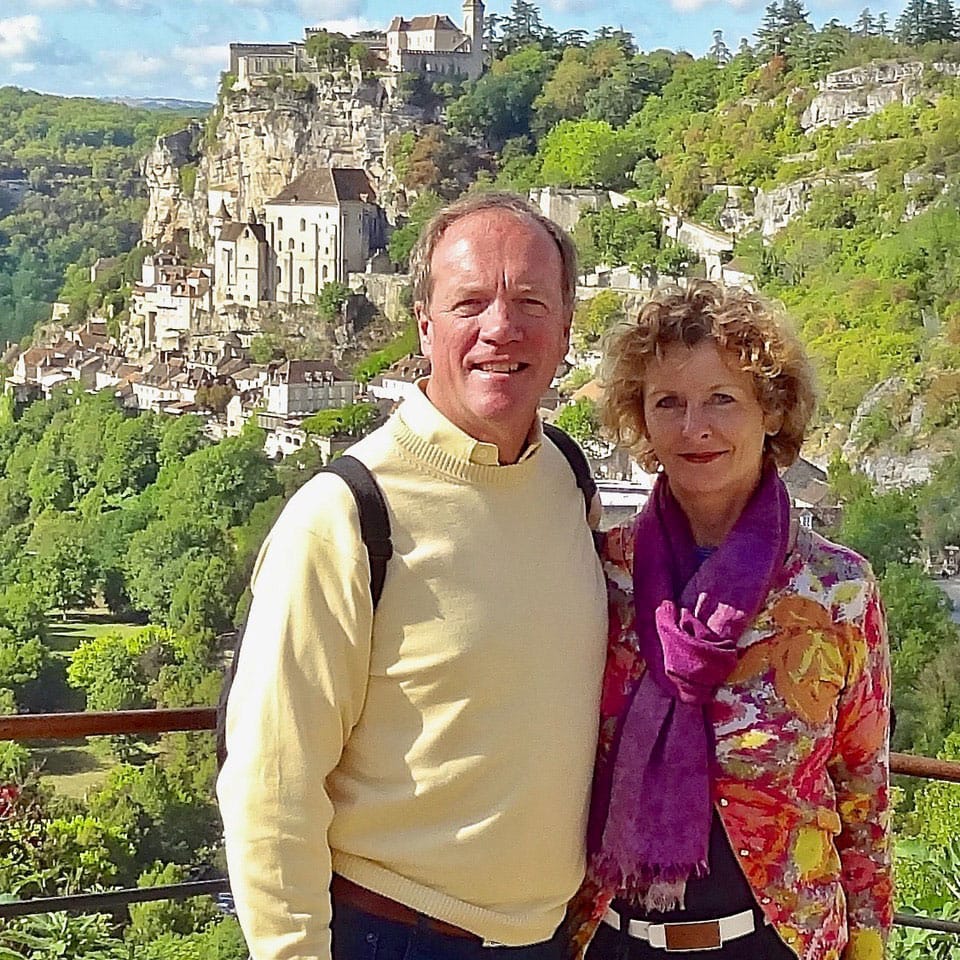 David and Louise Brace at a lookout point in David and Louise Brace in Rocamadour, France. Behind them, buildings cling to the sides of a steep rocky hill.