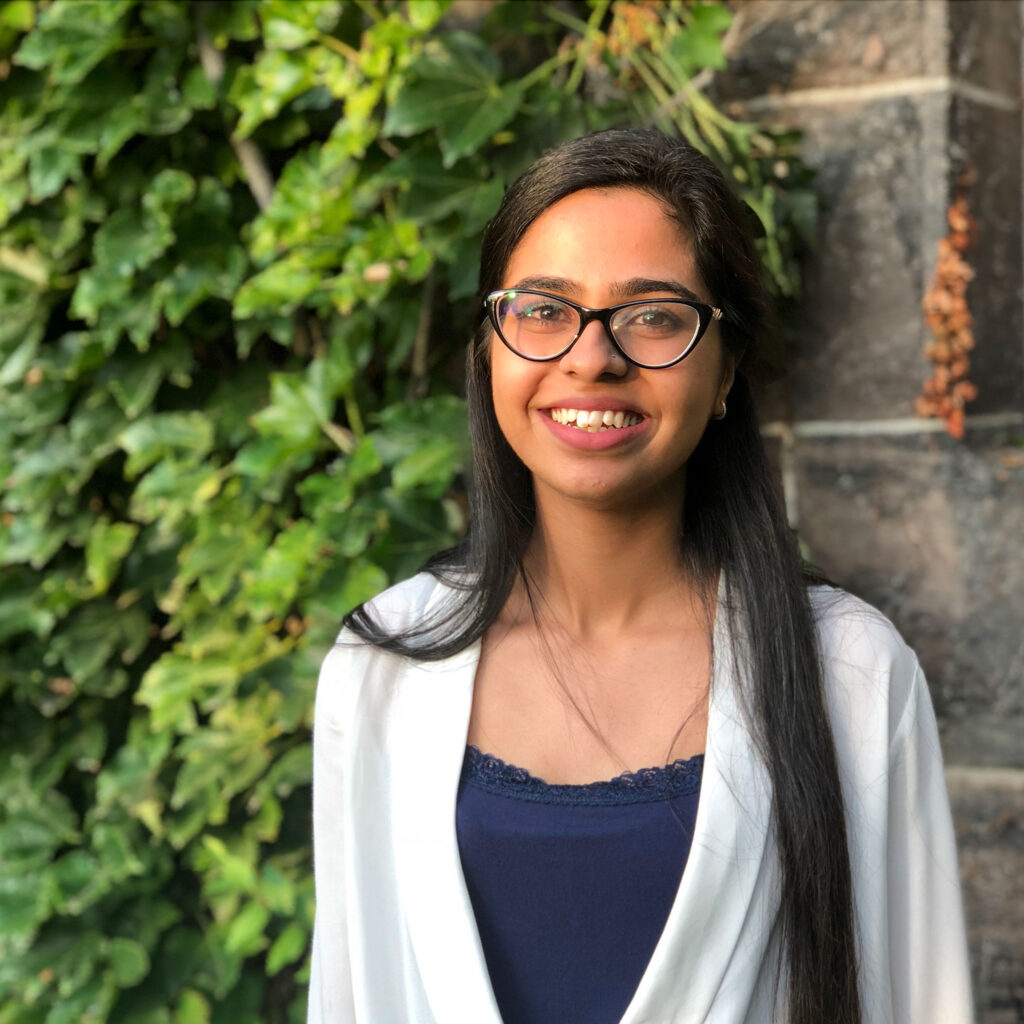 Khadija Rana smiles, standing outdoors by an ivy-covered wall.