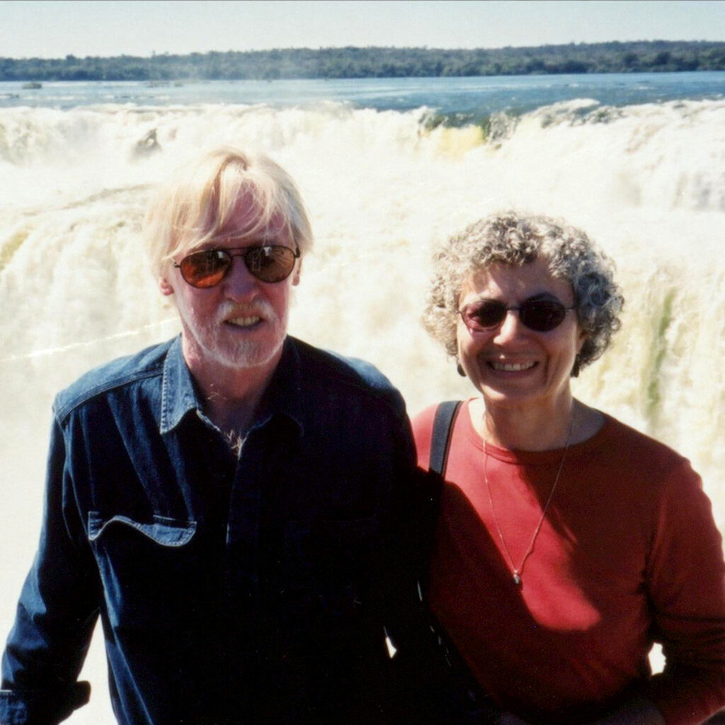 Marie Korey and Richard Landon stand in front of a spectacular, wide, 80 metres high waterfall.