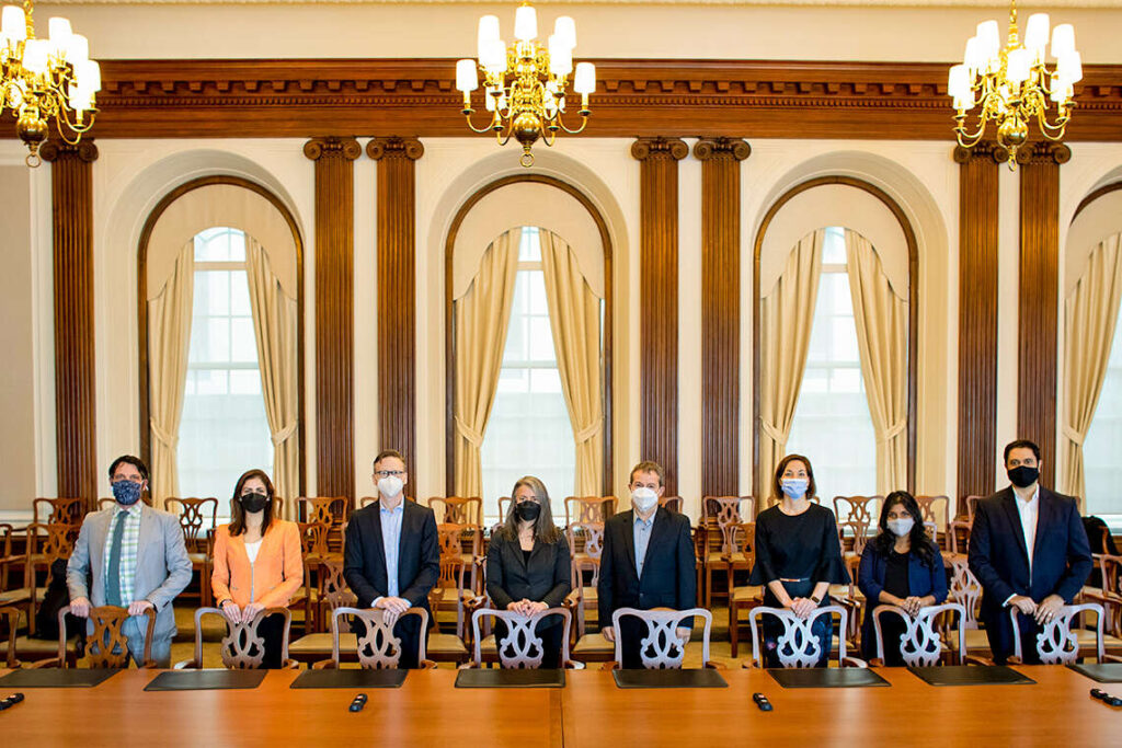 Eight people, wearing masks, pose for a picture in an elegant boardroom.