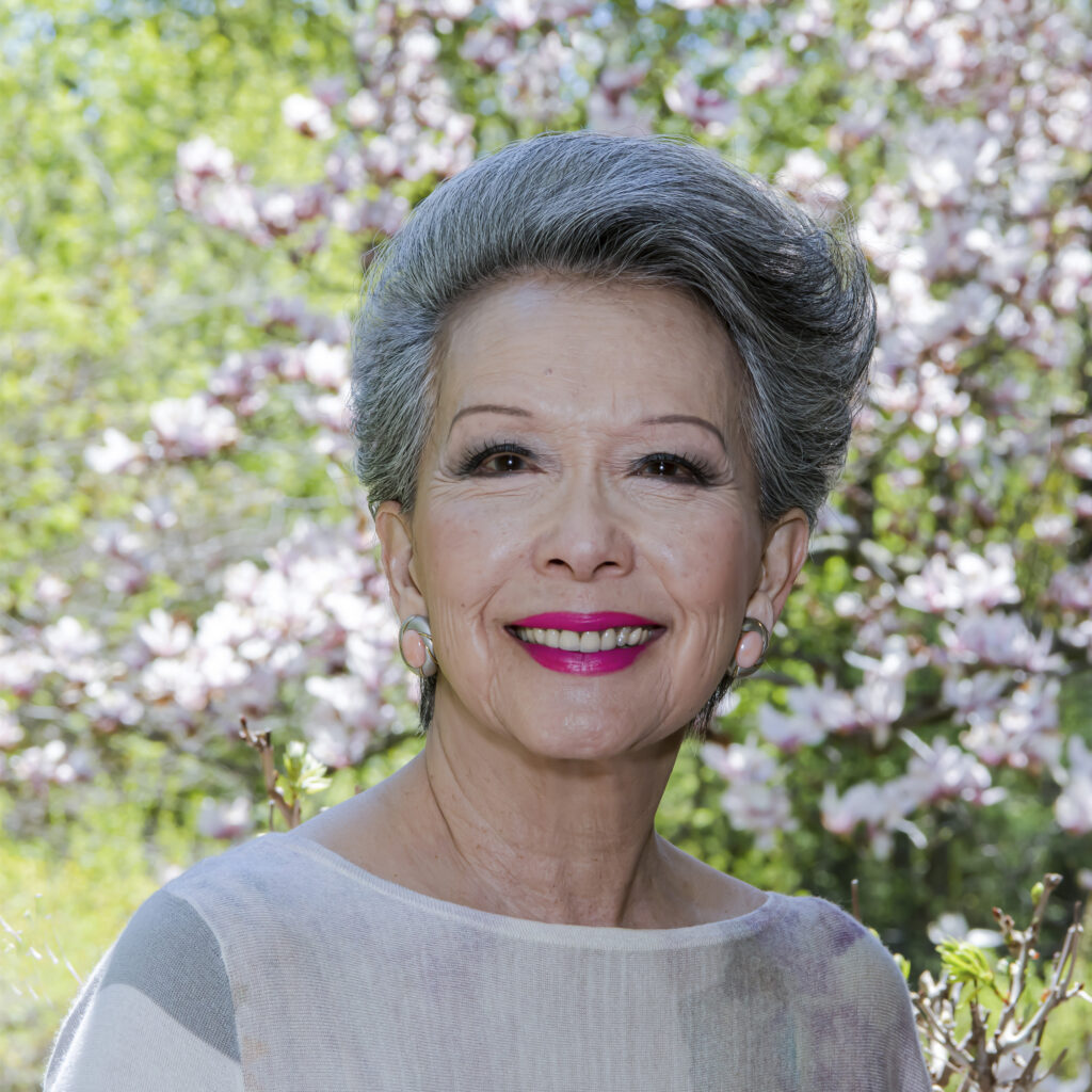 Vivienne Poy smiling and standing in front of a magnolia tree in blossom.