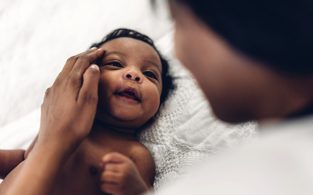 A happy baby smiles as a woman cradles the baby's face.