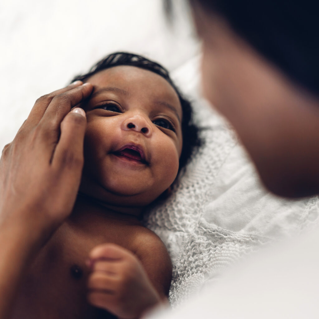 A happy baby smiles as a woman cradles the baby's face.