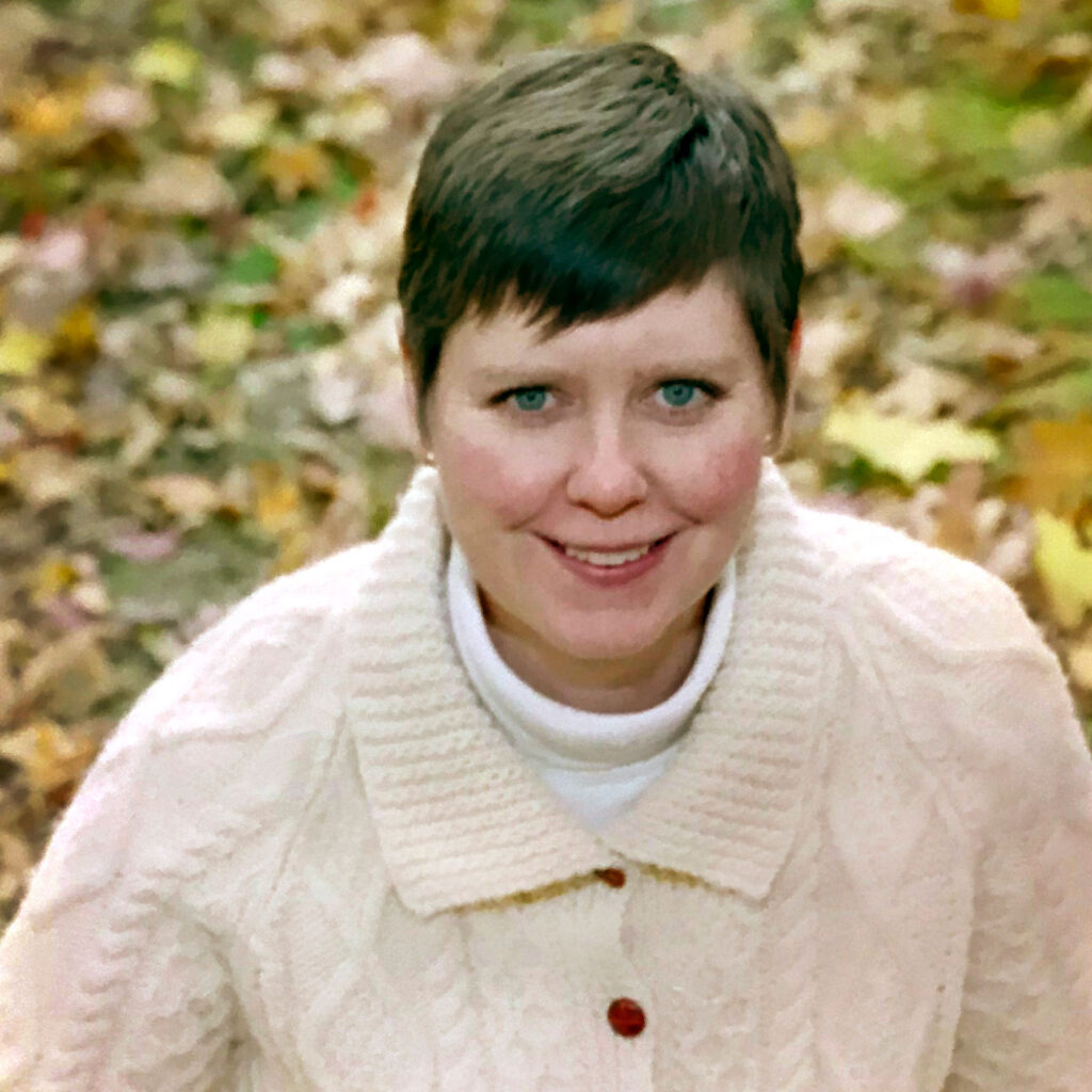 Jocelyn Whalen smiling, standing on a lawn covered in autumn leaves.