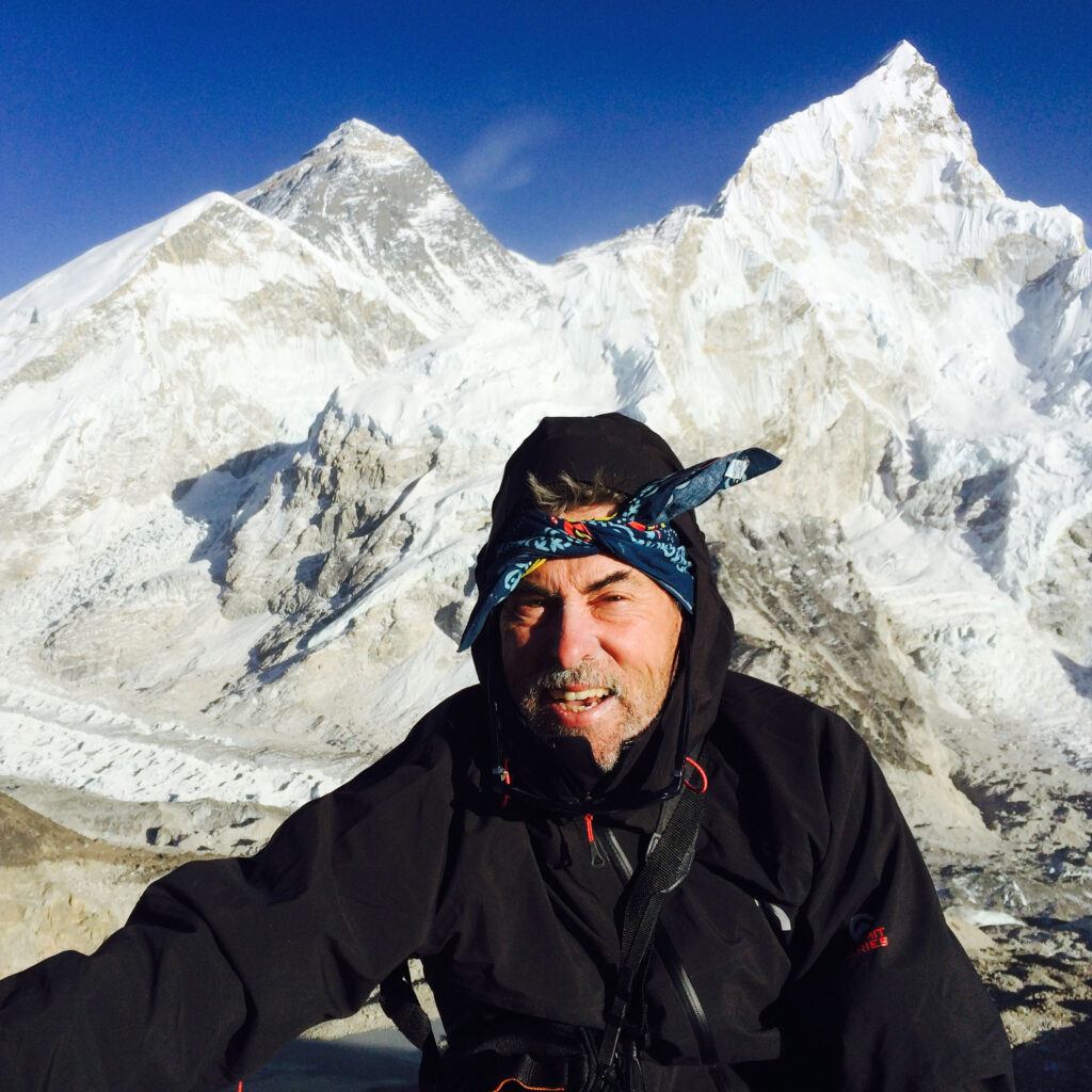 David Moore wears cold-weather gear. Behind him is a rocky valley and two snow-capped mountain peaks.